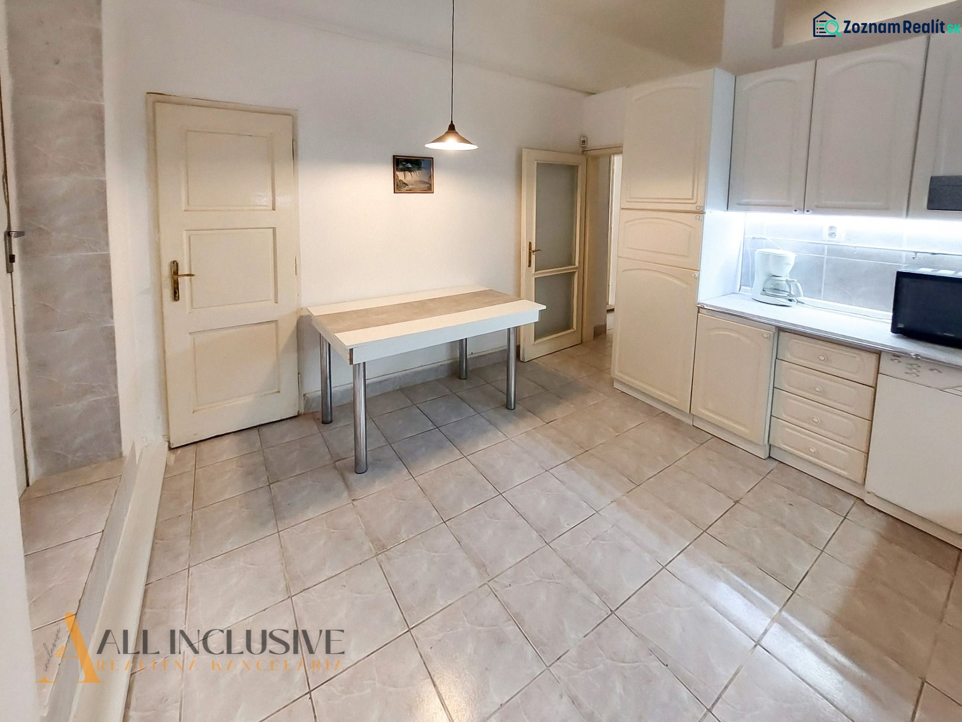 A kitchen in a 2-room apartment with white cabinets, a table, and tiles.