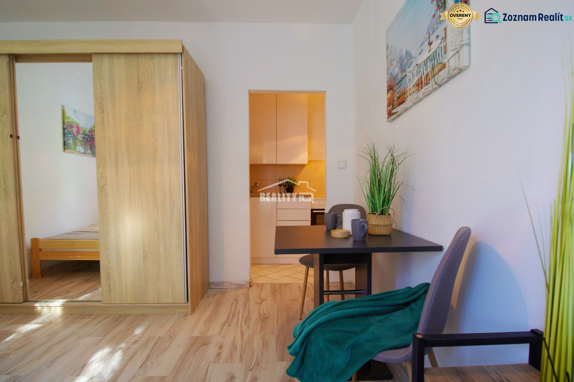 A studio apartment with a wooden floor, a table, and a plant, cozy furnishings.