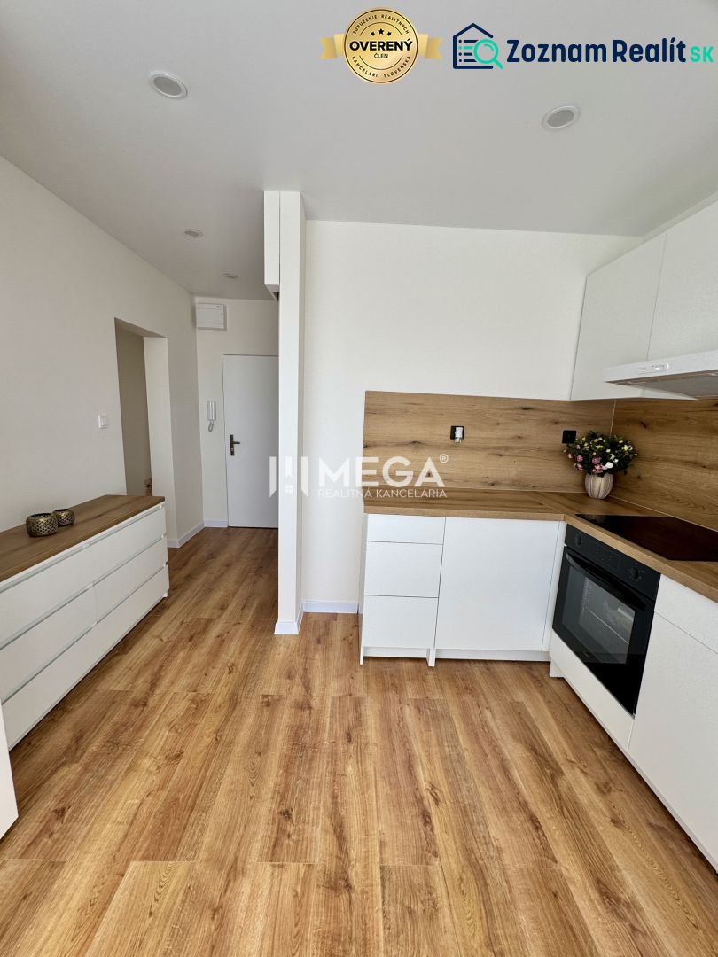 A kitchen in a studio apartment with white cabinets and a wood-patterned floor.