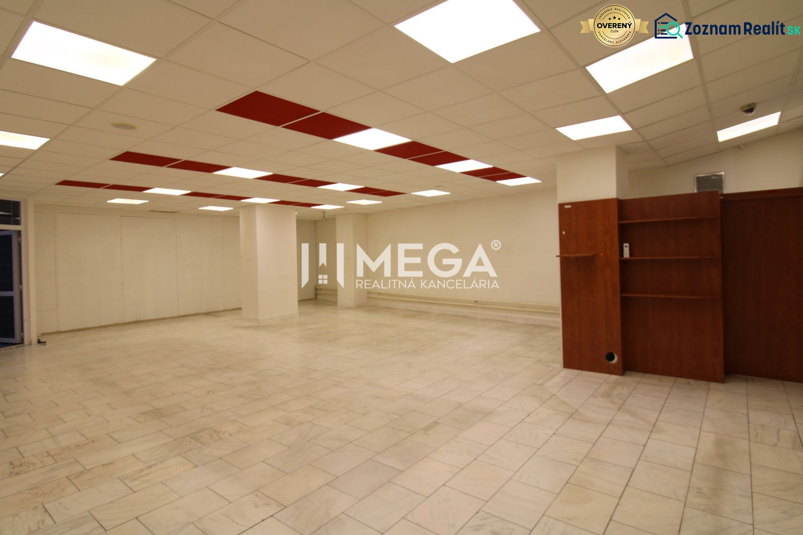 Interior of a commercial space with tiled flooring and ceiling lighting, shelves on the wall.