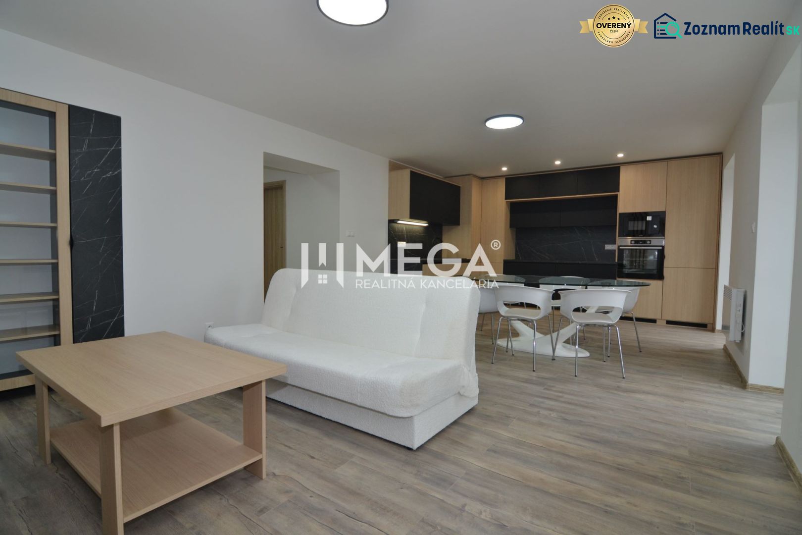 Living room in a three-room apartment with a wooden decor floor and a kitchen in the background.