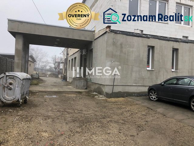 A building on SNP Street in Snina with a parked car and a container on a gravel surface.