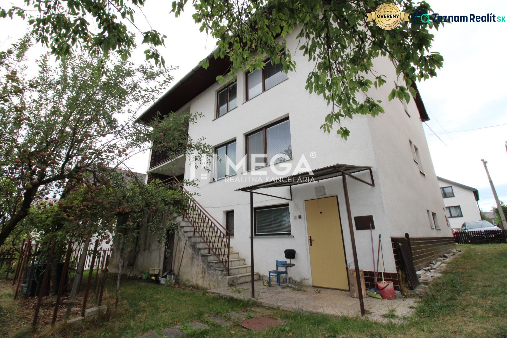 A family house on a street in Snina with two floors, trees, and an outdoor staircase.