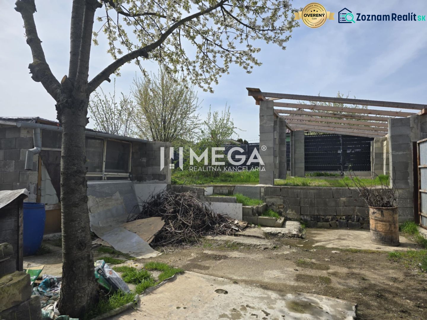 The courtyard of a family house in Sokoľany with a tree, building materials, and an unfinished structure.