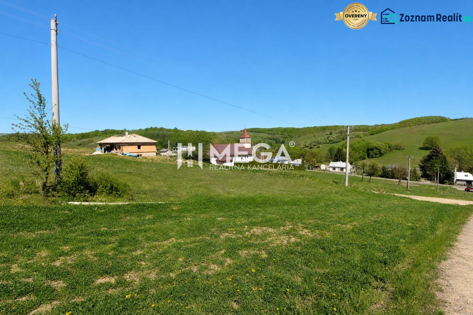 Grassy residential plots in the village of Víťazovce surrounded by green hills and buildings.