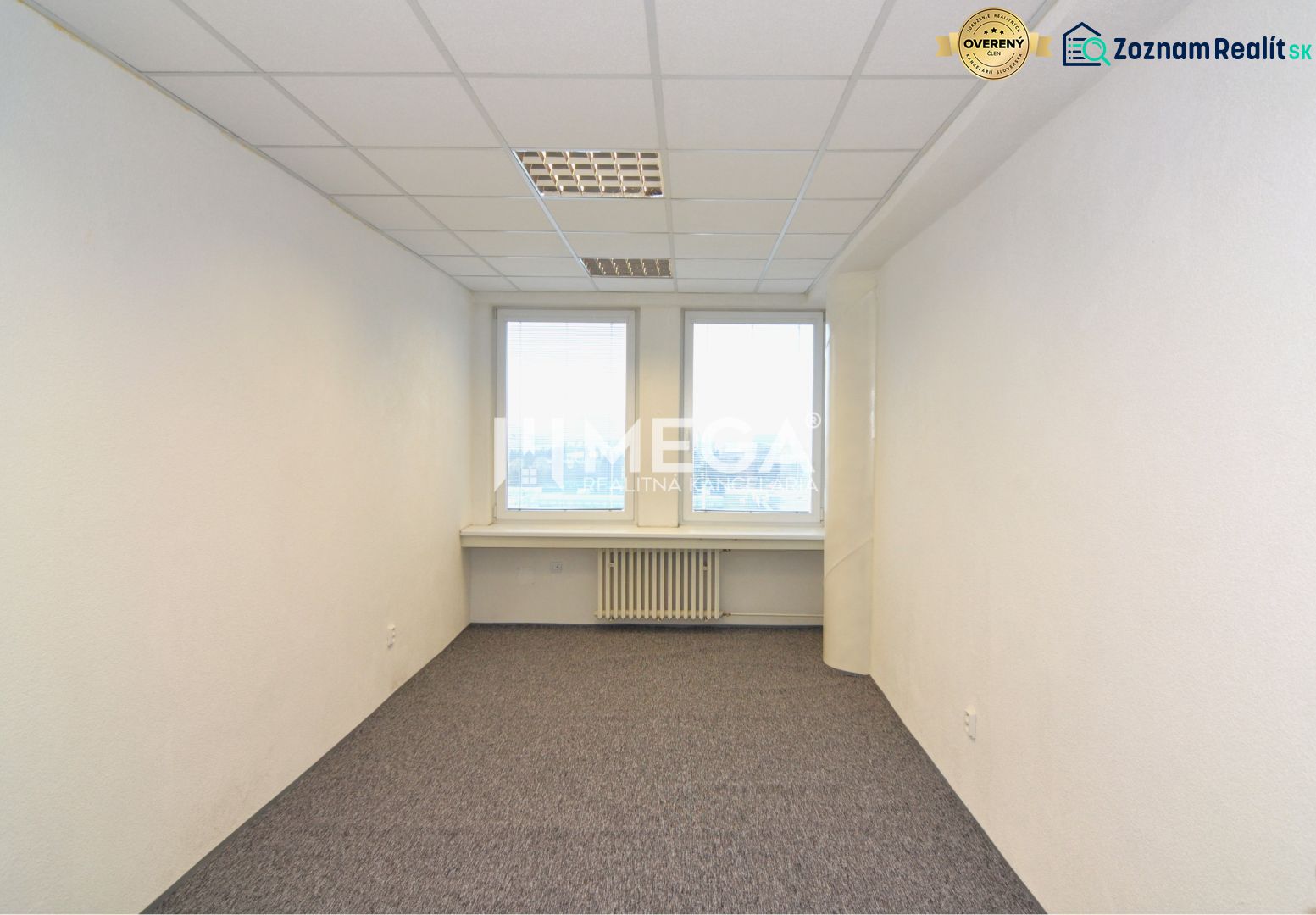 Interior of an office with white walls, carpet, and two windows.