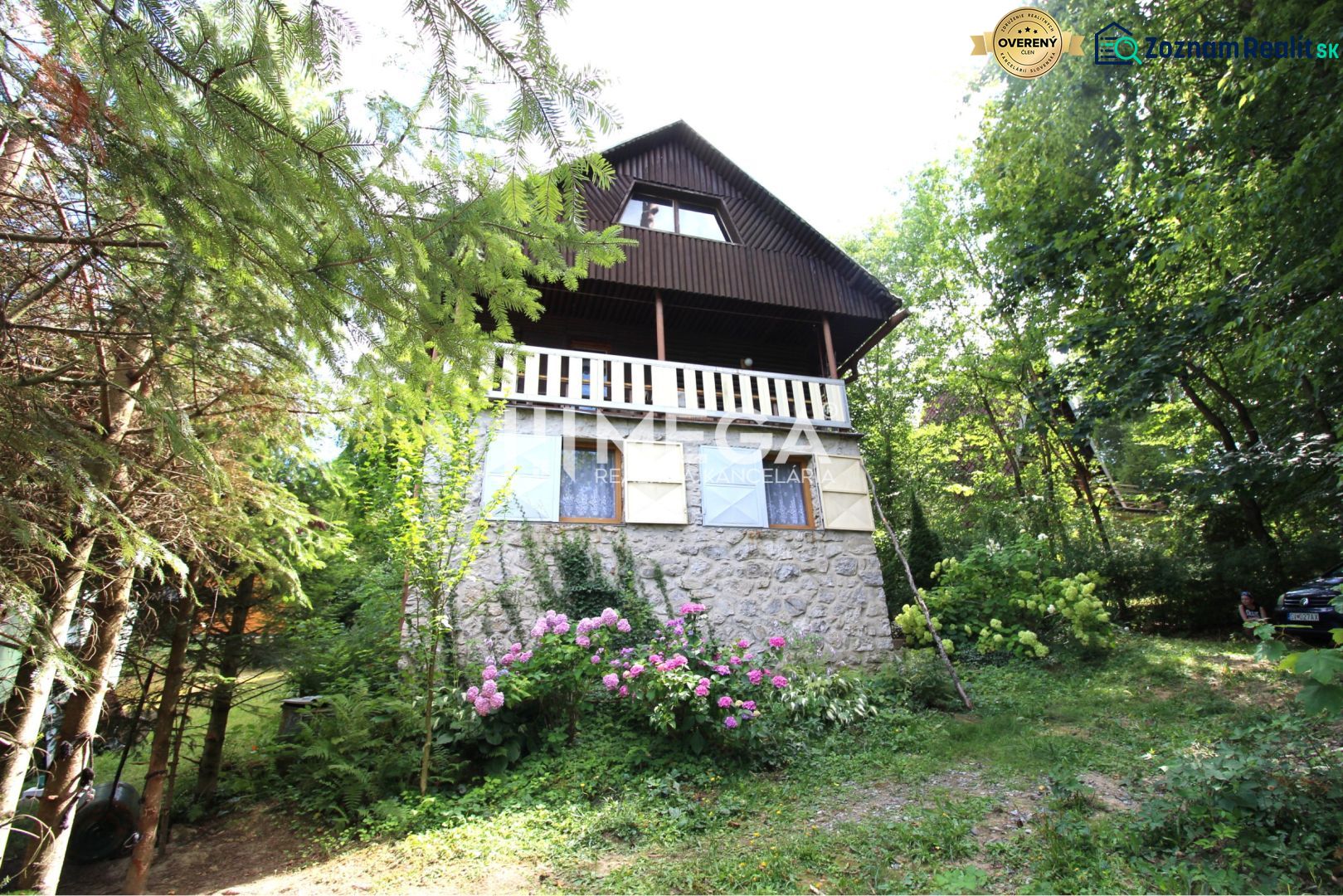A cottage in Holčíkovce surrounded by trees and flowers, with a stone lower part.