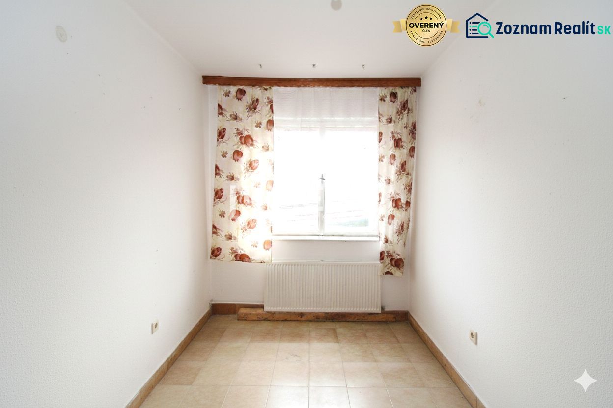 A room in a family house with a window, floral curtains, and tiles.