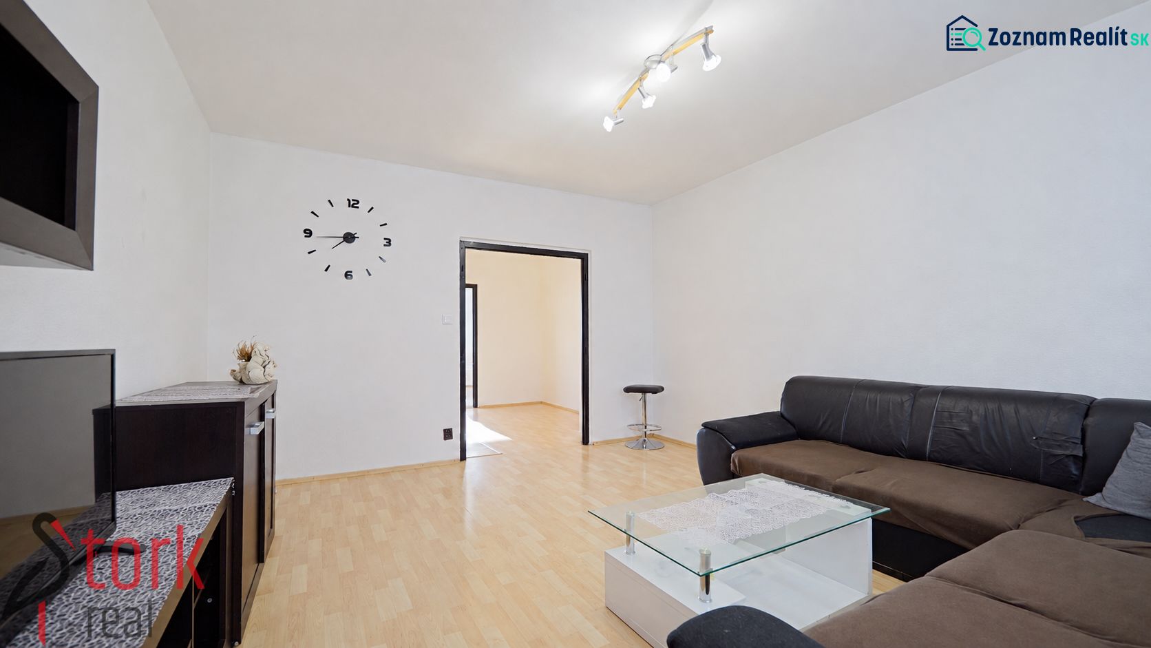 Living room in a three-room apartment with a sofa, glass table, and wooden decor flooring.
