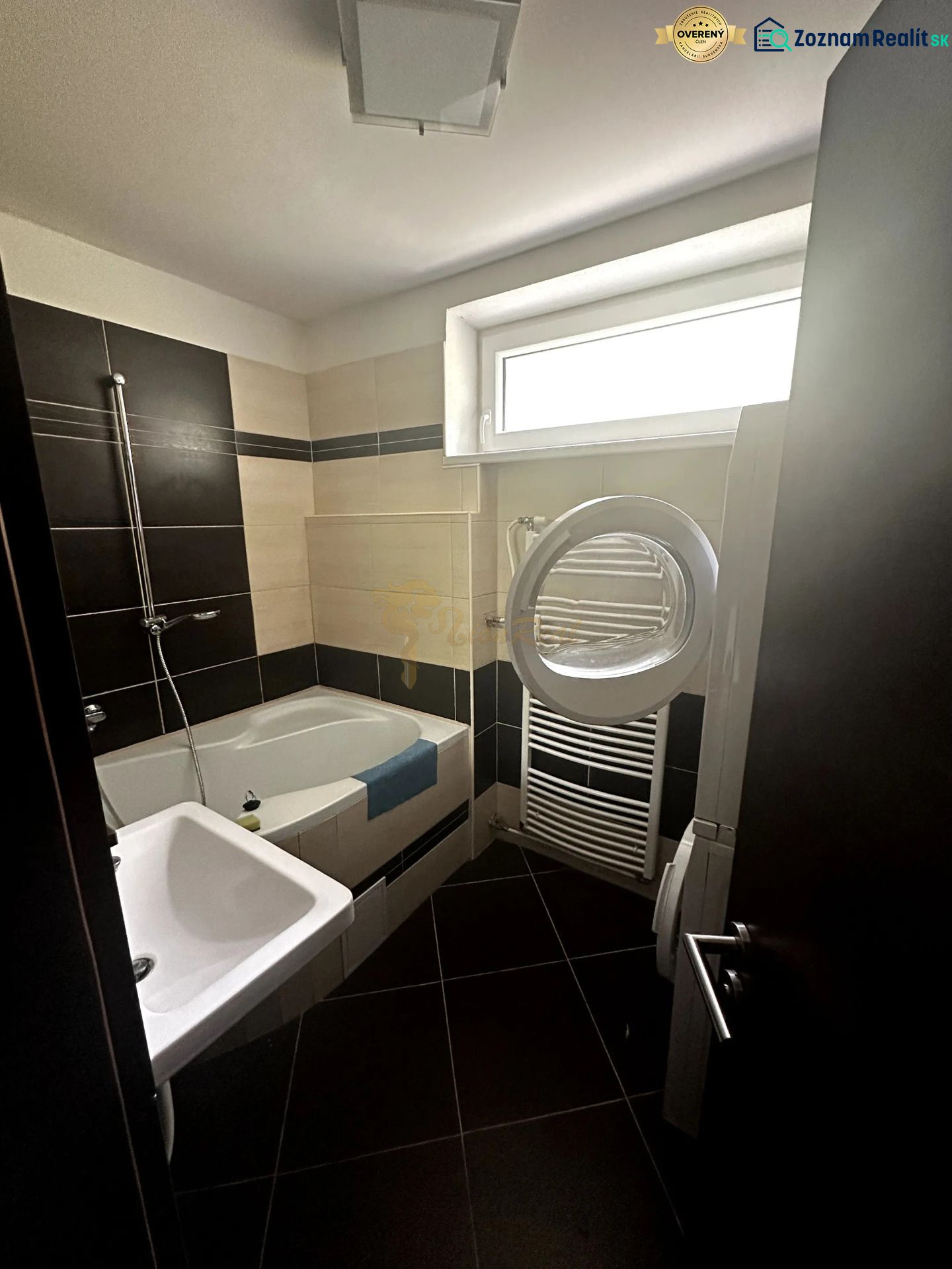 Bathroom in a 2-room apartment with a bathtub, sink, and washing machine; black and beige tiles.