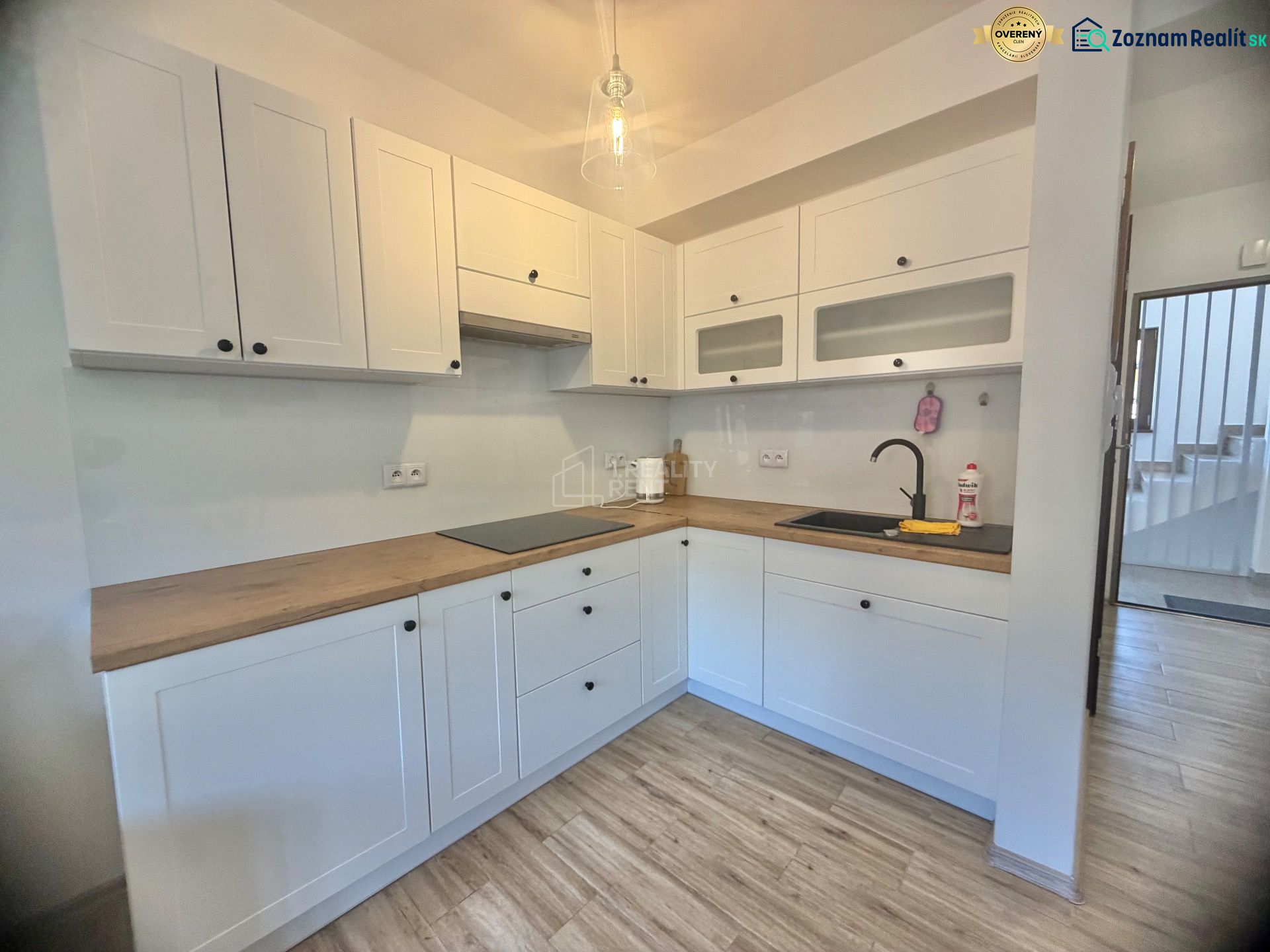 A kitchen in a studio apartment with white cabinets and a wood-patterned floor.