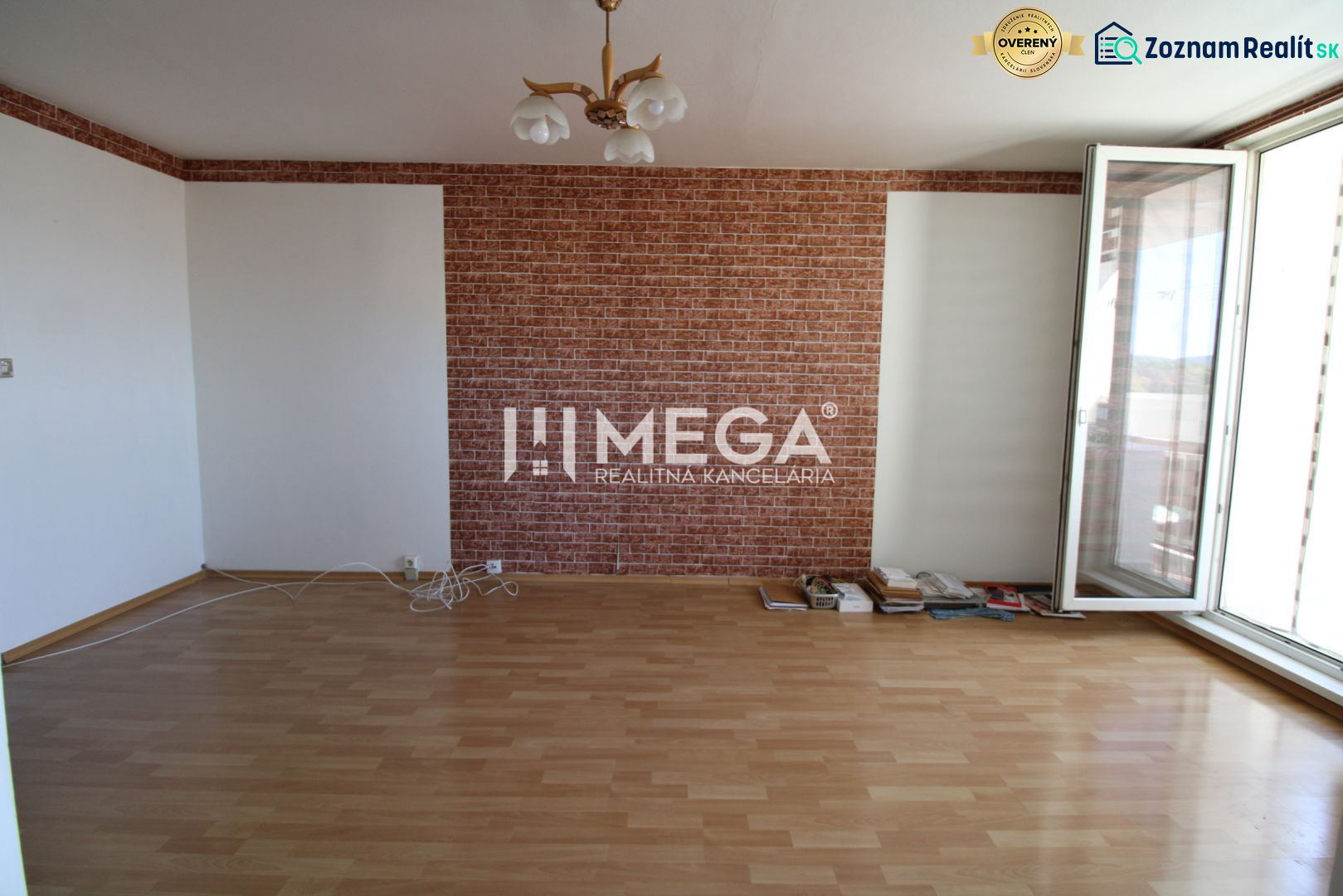 A room with brick cladding, a floor with a wooden decor, and a large window in a 3-room apartment.
