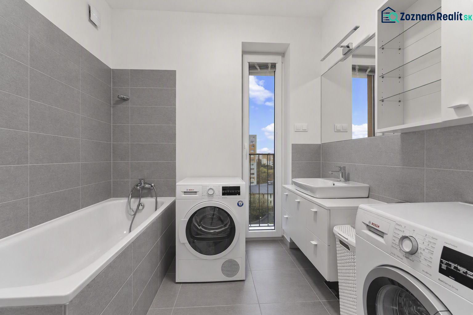 Bathroom with a bathtub, washing machines, and a sink in a 2-room apartment. Gray tiles, large mirror.