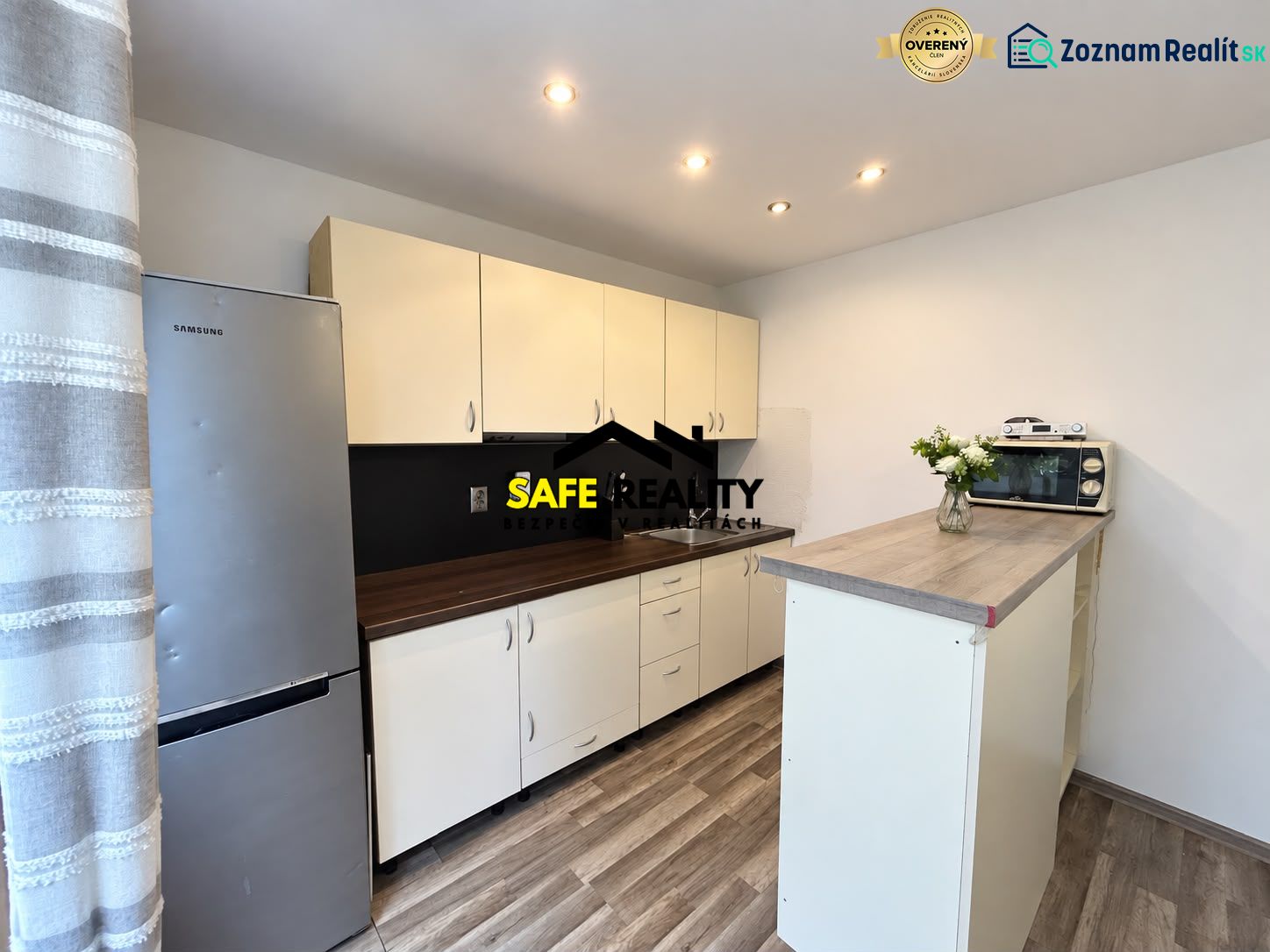 A kitchen with a wood-patterned floor, light cabinets, and a refrigerator in a studio apartment.