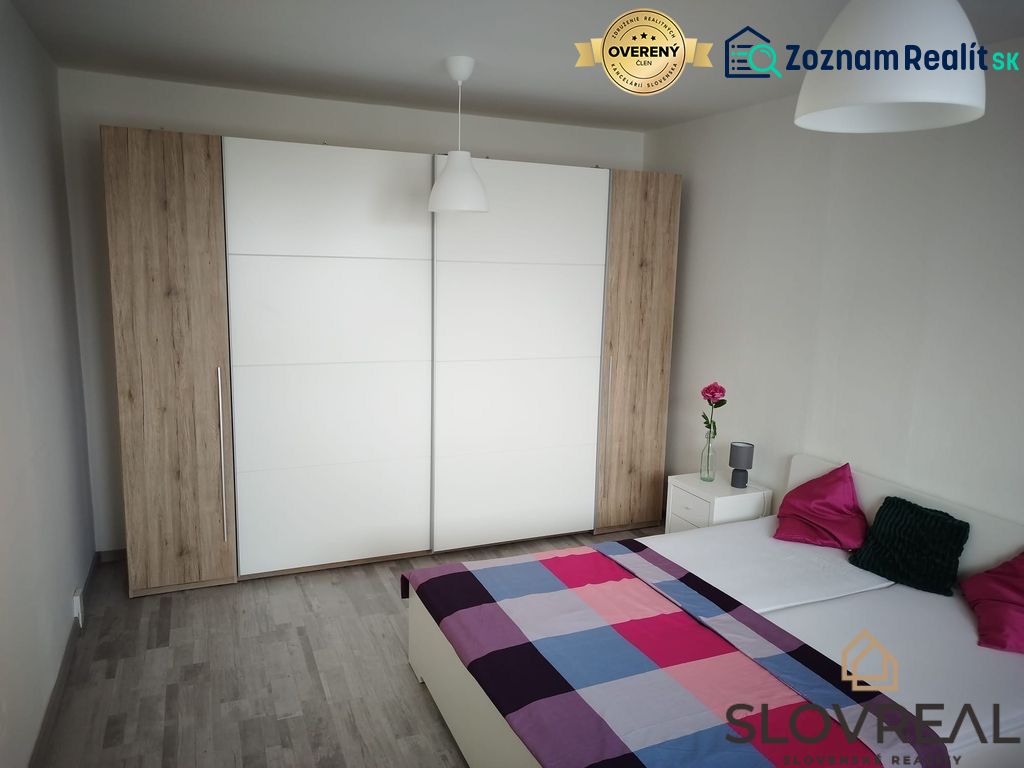 A bedroom with a wooden decor floor in a studio apartment, a wardrobe, and a bed.