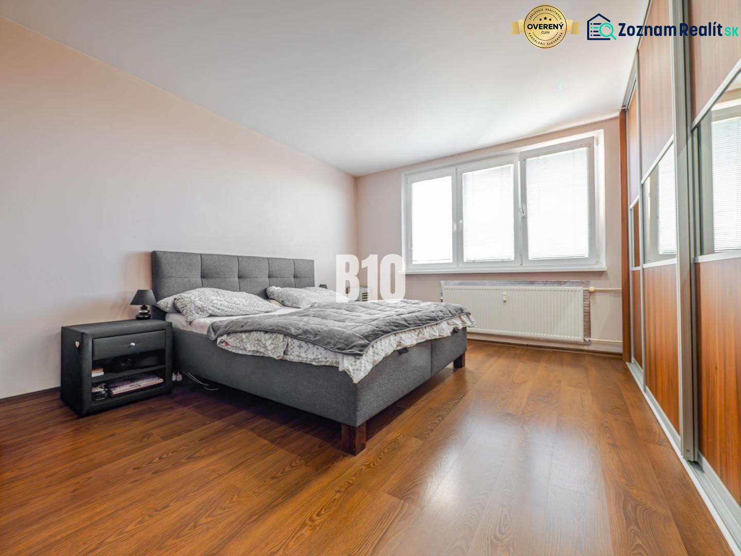 A bedroom with a large bed, a nightstand, and a wooden decor floor in a 3-room apartment.
