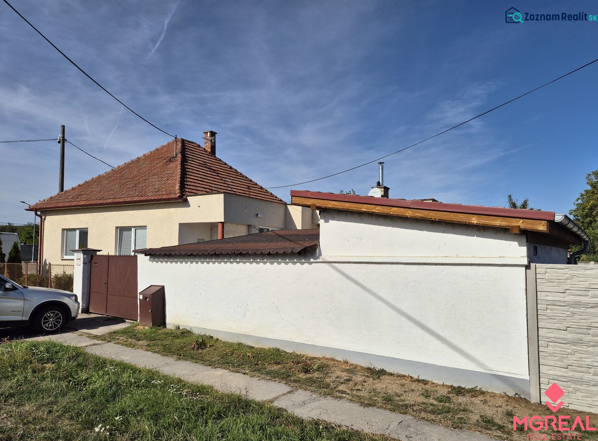 A family house in Ludanice with a sloped roof and fencing, with a parked car next to it.