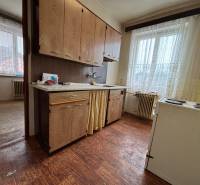 A kitchen in a 4-room apartment with older furniture, a window with white curtains.