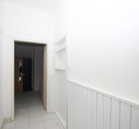 A white corridor leads to a room where a wardrobe with an oval mirror is visible.