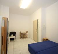 A simply furnished one-room apartment with a blue bed and a dining table.
