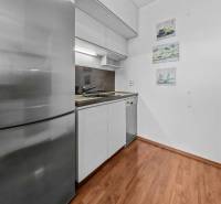 Kitchen area of a 2-room apartment with wooden flooring, a white kitchen unit, and a stainless steel refrigerator.