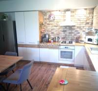 A kitchen in a 3-room apartment with a wooden floor, a brick wall, and built-in appliances.