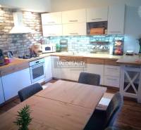 The kitchen in the 3-room apartment combines brick tiles, white cabinets, and wooden elements.