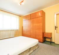 A bedroom in a 3-room apartment with a wooden wardrobe, yellow walls, and simple furniture.