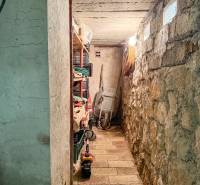 A stone cellar space with storage shelves and a wheelbarrow in a 3-room apartment.