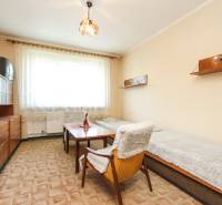 A room in a 3-room apartment with two beds, a chair, and curtains.