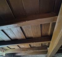 Ceiling of a rural family house with wooden beams and a stone wall.