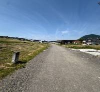 The road between residential plots in Gregorovce, with unfinished houses and mountains in the background.