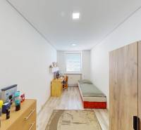 A room in a 3-room apartment with a bed, a table, a wardrobe, and a window at the end of the room.