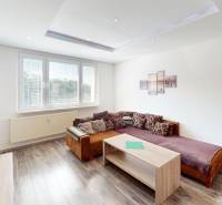 Living room in a three-room apartment with a sofa, coffee table, and open kitchen.