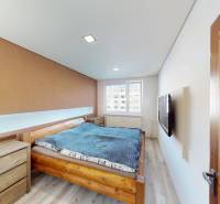 A bedroom in a 3-room apartment with a wooden bed, a dresser, and a TV on the wall.