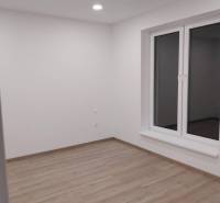 A minimalist room with wooden flooring, white walls, and a large window, located in a family house.