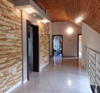 A hallway with stone cladding, a wooden ceiling, and stainless steel railing in a family house.
