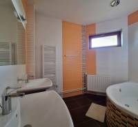 Bathroom in a family house with a shower, bathtub, and mirror, light tiles and a window.