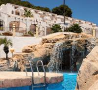 A waterfall by the pool in a recreational apartment in Calpe surrounded by palm trees and terraces.