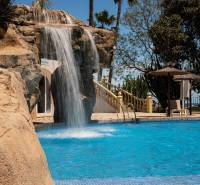 A pool with a waterfall and loungers in a holiday apartment in Calpe.