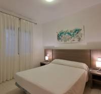 Bedroom in a holiday apartment with a double bed, wooden nightstands, and a painting.