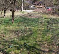 A grassy area near a stream with a house in the distance on Myslavská and Záhrady streets.