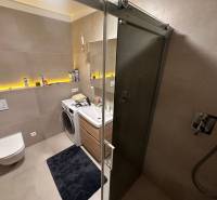 Bathroom in a 2-room apartment with a shower, washing machine, and toilet, with decorative lighting.