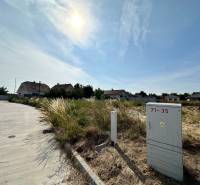 Plots - housing in Slovenská Nová Ves with a road and an electrical box on a sunny day.