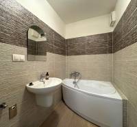 A bathroom with a corner bathtub and a sink in a 3-room apartment, surrounded by tiles.