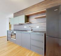 A kitchen in a 2-room apartment with gray cabinets, a stove, and wooden flooring.