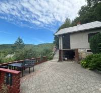 In the picture, there is a countryside cottage surrounded by nature with a terrace and a view of the forests.