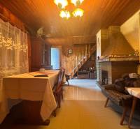 The interior of a wooden cabin with a fireplace, staircase, decorative curtains, and wooden furniture.