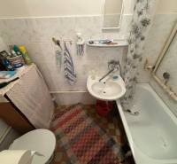 A small bathroom in a cottage with a bathtub, sink, mat, and curtain.