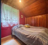 A bedroom in a wooden cabin with a double bed and a window with white curtains.
